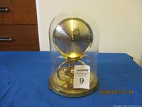 Full view of Kundo anniversary clock encased in a glass dome on a blue cloth, showing overall condition and presentation.