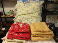 Full overview of the linens set including floral ruffled pillow cases, red and yellow bedding linens folded.