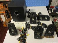 Photo showing the subwoofer, four satellites, center speaker, and connected wires bundled together on a white surface.