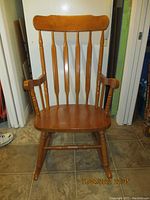 Front view of wooden rocking chair showing curved backrest with vertical spindles and armrests.