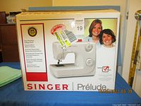 Front of retail box showing Singer Prelude sewing machine, model details, and branding.