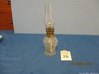 Front view of the small vintage clear glass oil lamp showing ornate embossed design and brass burner with chimney.