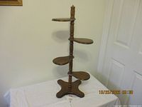 Full view of wooden plant stand showing four tiered shelves, turned central support column, and wide rounded base.