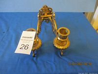 Photo shows a pair of solid brass wall candle holders placed on a blue cloth background from an angle showing the side and front of the items.