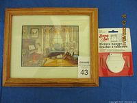 Framed print of a living room scene with dog and wooden frame, including MaxSold tag and packaged picture hanger hardware