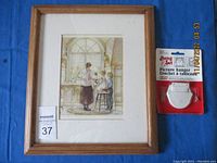 Framed picture showing woman and children by window with original picture hanger beside it on blue surface.