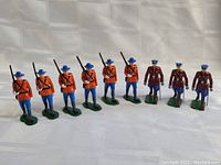 All nine vintage soldier figures in a line showing six Mounties in red and three police in maroon with blue hats.