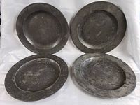 Four antique pewter plates including two round and two oval shapes on a white background.