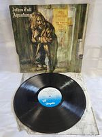 Photo showing the vinyl LP record on a white surface with the original cover sleeve behind it. The record shows some surface reflections indicating it is in good condition, the label is blue Chrysalis.