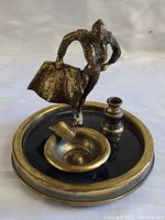 Photo showing metal ashtray with bullfighter matador figurine standing on a round base with cigarette rest and candle holder.
