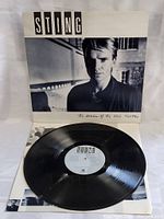 Vinyl LP record removed from sleeve, showing the record and label, with album cover in the background.
