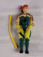 Front view of the vintage G.I. Joe female action figure in green and yellow outfit with red hair and yellow bow accessory.
