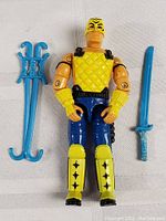 Front view of Vintage Hasbro G.I. Joe action figure with blue and yellow outfit and accessories (sword and grappling hook)