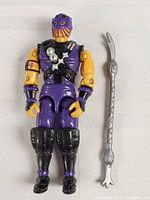 Front view of vintage G.I. Joe action figure dressed in purple, yellow, and black with matching silver weapon accessory.