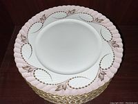 Stack of 11 Royal Tettau dinner plates showing pink scalloped edges with gold detailing.
