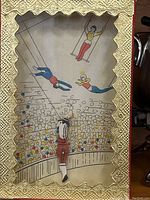 Front view of Shackman Flying Trapeze Toy featuring trapeze artist figure in red pants inside a glass box with illustrated circus background and ornate gold trim.