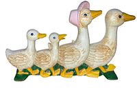 Front view of cast iron gaggle of geese doorstop showing four geese painted white with yellow beaks and feet, one with pink bonnet on head.