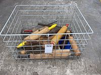 Wire basket filled with multiple wooden rolling pins and kitchen utensils placed on concrete floor.