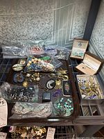 Top-down view of tray holding assorted costume jewelry including bracelets, necklaces in plastic bags, earrings, and pendants laid out for display.