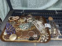 Tray of assorted costume jewelry laid out, showing mixed necklaces, bracelets, earrings, and brooches with various beads and metal tones.