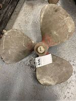 Top view of three-bladed bronze ship propeller on concrete floor with auction tag attached.