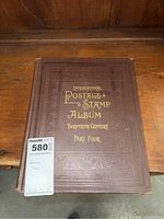 Front cover of an old postage stamp album with embossed brown cover and gold lettering showing the title 'International Postage Stamp Album Twentieth Century Part Four'.