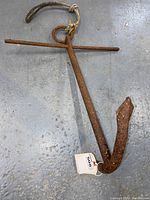 Front view of the rusty iron spade tip anchor showing the shaft, crossbar, rope loop, and spade tip.