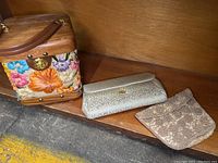 Three vintage purses displayed on a wooden shelf, showing wooden top floral purse, silver clutch, and beaded purse.