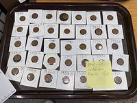 35 Wheat Pennies from the 1940s and 1950s in holders laid out on a tray. Each coin is in a white cardboard holder with handwritten dates and some mint marks.