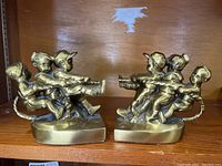 Pair of brass bookends shaped as children playing tug of war displayed on wooden shelf.