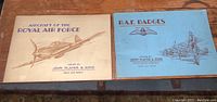 Two vintage cigarette card booklets, one blue titled 'R.A.F. Badges' and cream titled 'Aircraft of the Royal Air Force', both issued by John Player & Sons
