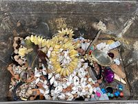 Photo of the open tin containing various costume jewelry pieces including shell necklaces, beads, and large pendants.