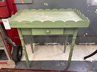 Full front view of vintage green wooden table showcasing scalloped edges and a single drawer with round knob.