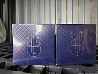 Photo showing two sealed blue boxes, each containing a pair of wireless white earbuds with charging case, depicted by the line drawing on the front of each box.