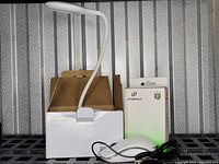 Photo shows white LED Innovativ desk lamp standing partially out of its white packaging with cardboard background; Jitopkey wired mouse box visible behind lamp with lamp power cord and mouse USB cable coiled in front.