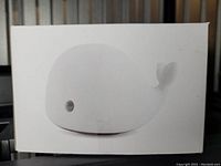Photo of the Dolphin Light box showing a white silicone dolphin shape light with an eye and tail detail, minimalistic design.