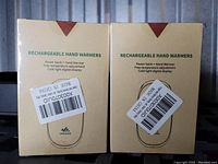 Image showing the front of two unopened beige boxes labeled Rechargeable Hand Warmers with product details and barcodes