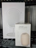 Photo of the boxed white LED light up makeup mirror and boxed beige USB mini bottle humidifier together on a shelf.