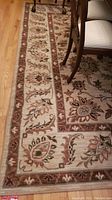Partial close-up of the cream and brown patterned edge of the rug alongside chair legs on a hardwood floor.