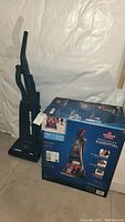 Photo of Eureka The Boss upright vacuum and Bissell Proheat Essential deep cleaner box side by side on floor in a basement with white walls.