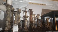 Wide view showing fourteen candle holders of different sizes and materials placed on a shelf in a basement setting.