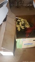 Box containing artificial white poinsettias with green leaves and red bows along with other artificial Christmas greens.