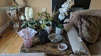 Overall display of all items including vases, faux florals in pottery look planters, metal serving plate on marble table