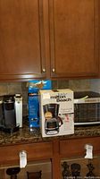 Photo showing Keurig coffee maker, Milton Beach coffee maker box, and Black and Decker appliance next to toaster oven on kitchen counter.