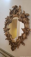 Front view of the ornate gilt wood framed mirror hanging on a wall, showing detailed scroll and leaf carvings in a gold finish.