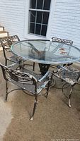 Full set of patio furniture with glass-topped table and four metal armchairs showing weathered paint
