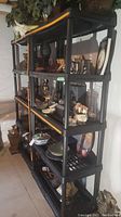 Photo showing two black plastic shelving units side by side with multiple household items on shelves in basement area.