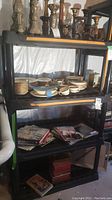 Front view of the black plastic shelving unit with various household items on shelves (not included).