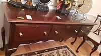 Front view of wooden server displaying four drawers with brass pulls and curved legs, placed on a patterned rug with decorative items on top