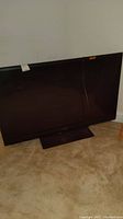 Full view of Sharp 52 inch television standing on carpeted floor with stand attached.